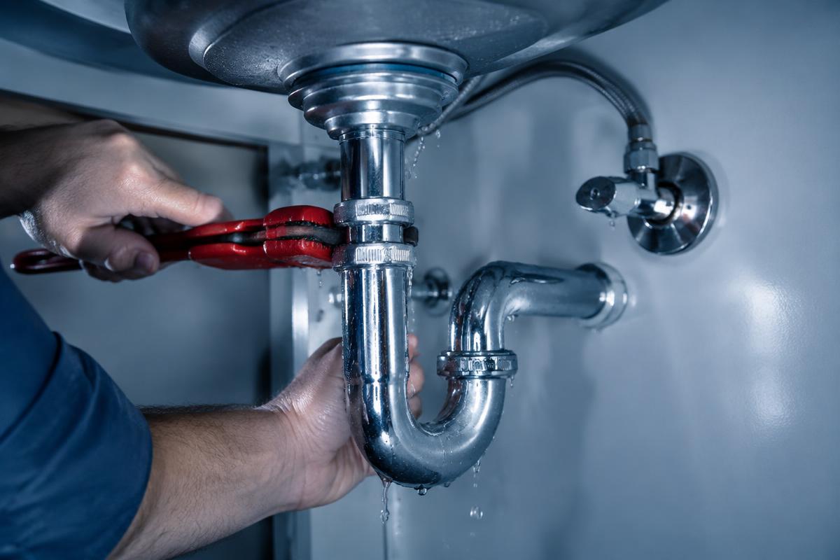 Plombier réparant une fuite sur un siphon sous un évier
