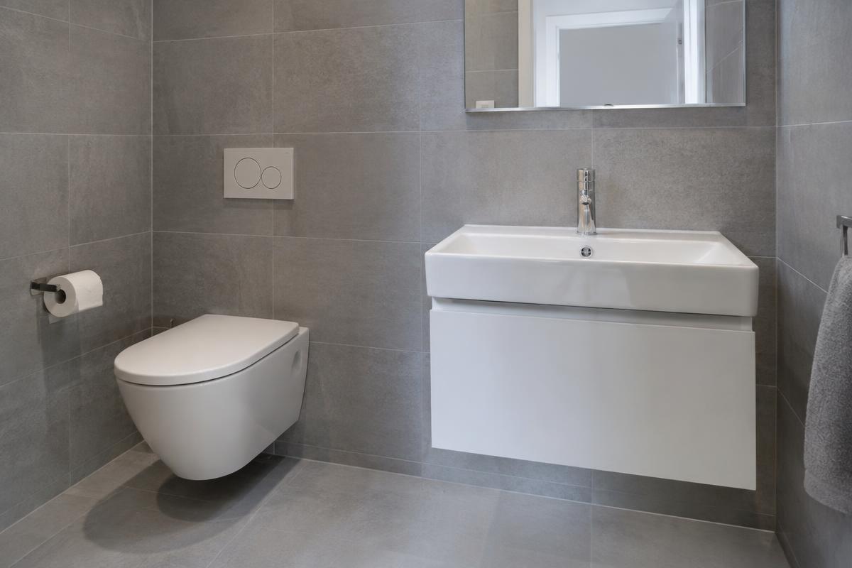 WC suspendu et lavabo installés dans une salle de bain carrelée grise